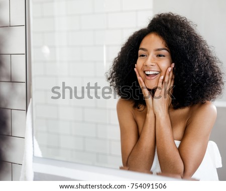 Happy woman admiring her skin in front of the bathroom mirror, touching face with hands Royalty-Free Stock Photo #754091506