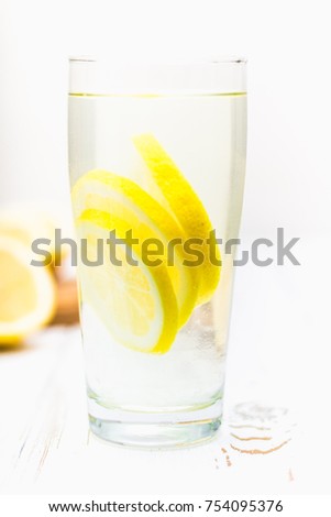 A glass beaker and a jug of cold lemonade on a white wooden background surrounded by lemons