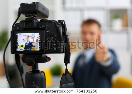Male in suit and tie show confirm sign arm making promo videoblog or photo session in office camcorder to tripod closeup. Vlogger promotion selfie solution or finance advisor management information