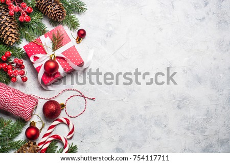 Christmas background or xmas greeting card. Red christmas present box, fir tree branch and decorations on gray stone table. Top view with copy space.