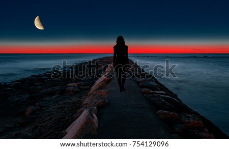 Silhouette of a woman walking by the sea at night Royalty-Free Stock Photo #754129096