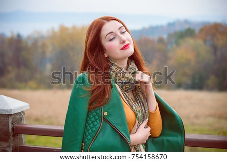 Girl with red hair and red lips, dressed in a green leather jacket and scarf casual style, resting in a pleasant place is in a sense of peace and harmony. Beauty in every day and moment, the pleasure 