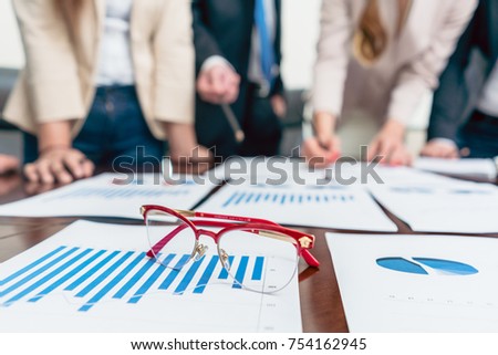 Close-up of eyeglasses with red frames on a printed bar chart showing progress during a meeting of business analysts, in the office of a successful company