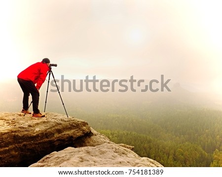Photographr looking into viewfinder of dslr digital camera stand on tripod. Artist  photographing mountain and cloudy landscape.  Man check picture on screen his dslr camera while shooting pictures