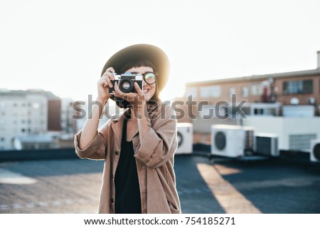 Amazing and inspirational shot of young creative soul or artist posing or making photo with vintage analog retro camera on rooftop full of warm summer sunlight flares, cute and beautiful woman