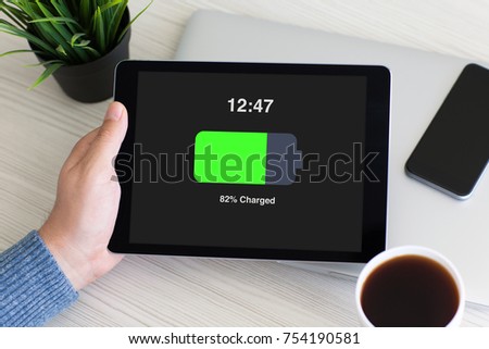 man hand holding computer tablet with charged battery on screen over table in office