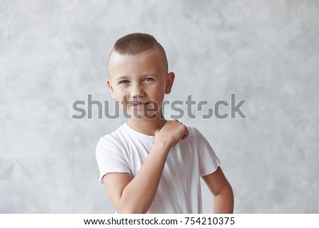 I will cut off your head. Picture of outraged little male hooligan in white t-shirt warning his enemy, gesturing with finger at his neck, standing at blank studio wall with copy space for your text Royalty-Free Stock Photo #754210375