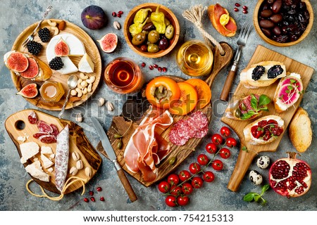 Appetizers table with italian antipasti snacks and wine in glasses. Brushetta or authentic traditional spanish tapas set, cheese variety board over grey concrete background. Top view, flat lay Royalty-Free Stock Photo #754215313