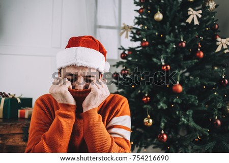 Cozy and nice picture of a guy wearing traditional Christmas clothes. Young man is sitting on the floor hear beautiful and green pine tree and relaxing. He is full of calm, joy and happiness. Cut view