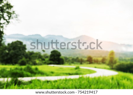 Blurry grass nature field with car road way in weather rainy cloudy day vintage picture style countryside of Thailand.