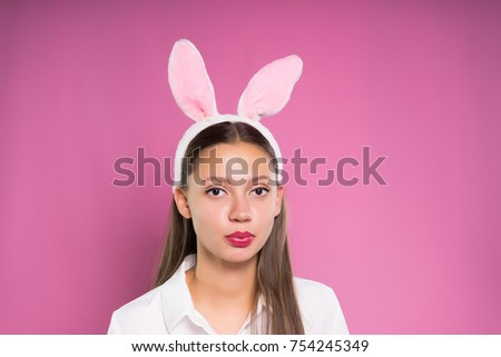 charming young girl in a white shirt, with a rim in the form of rabbit ears on her head trying to inflate a bubble of chewing gum
