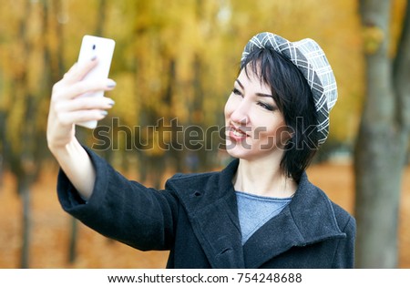 girl taking photo on the phone in autumn city park, yellow leaves and trees, fall season