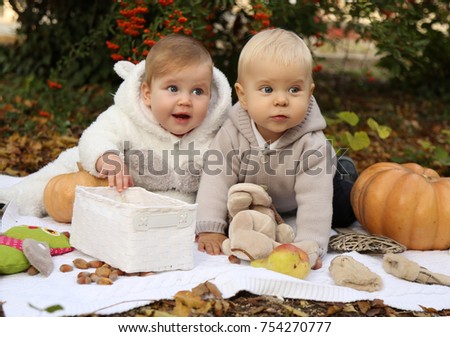 outdoor photo of small children posing with pumpkin and toys among trees in autumn park