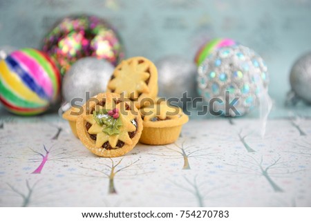 Christmas food photography picture with traditional pastry fruit mince pies with holly iced top and colorful bauble tree decorations with white shiny seasonal background in tree patterns