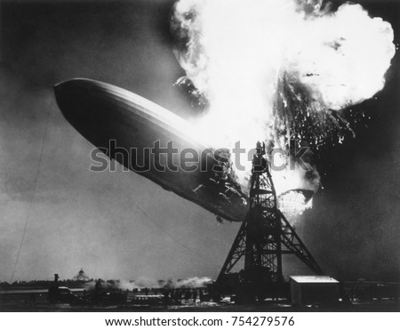 The German passenger airship Hindenburg seconds after catching fire, May 6, 1937. At 200 feet above the ground, flames erupt on top and in the back of the ship. It descended as it burned, reaching the Royalty-Free Stock Photo #754279576