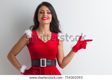Pretty Pin-up style Santa girl in red hat pointing to white background