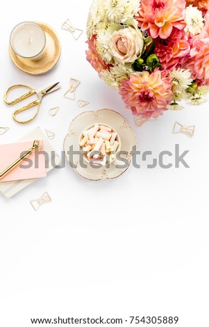 Flat lay women's office desk. Female workspace with pink roses flowers bouquet, accessories on white wooden background. Top view feminine background.