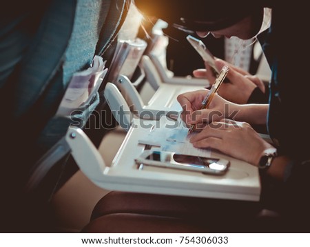 Tourist hand filling Immigration form on flight to visit country. A man is writing/signing on a paper.Man passenger Write Immigration Card in Airplane