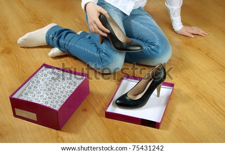 Girl sitting on the floor and gets  the black shoes out of the box
