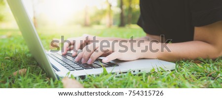 Young asian woman's legs on the green grass with open laptop. Girl's hands on keyboard. Distance learning concept. Happy hipster young asian woman working on laptop in park. Panoramic banner.