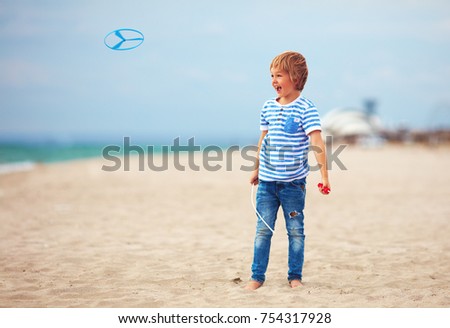 delighted cute young boy, kid having fun on sandy beach, playing leisure activity games with propeller toy