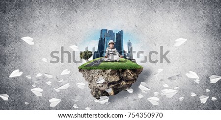 Young little boy keeping eyes closed and looking concentrated while meditating on island in the air among flying paper planes with gray wall on background. 3D rendering.