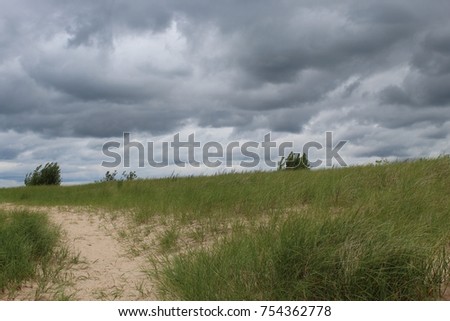 A storm rolling over a sand dune covered landscape with storm clouds in the distance in Michigan