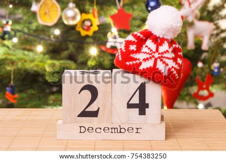Date 24 December with woolen red cap and festive tree with lights and decoration in background, Christmas eve time concept Royalty-Free Stock Photo #754383250