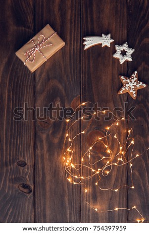 Christmas gift, decorated gingerbread cookies and Christmas lights on the old wooden table, decorated by festive decor. Dark rustic style. Top view.