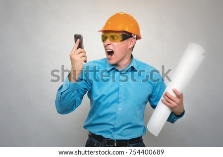 An angry disgruntled engineer worker in a helmet with project drawings plans in his hand yells and screams in mobile phone on someone. Bad executed work.