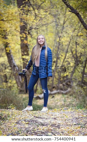 Cute blonde smiling teen girl holding her camera taking photos during a beautiful fall day outdoors. Teen having a fun with her artistic hobby