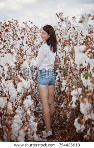 Young attractive girl stand among the harvesting cottong white bushes on the field. Fashion and textile industry concept. Light and clear picture