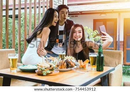 Two Asian women and one men hand holding mobile phone Taking pictures with  food on table 