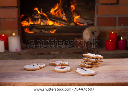 Christmas cookies or gingerbreads on wooden table beside cosy open fire place. Winter holidays concept, horizontal