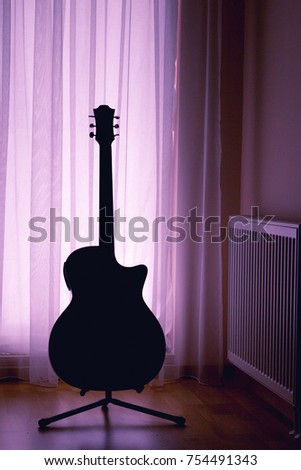 silhouette of an acoustic guitar on a light background of curtains and a large window of a house