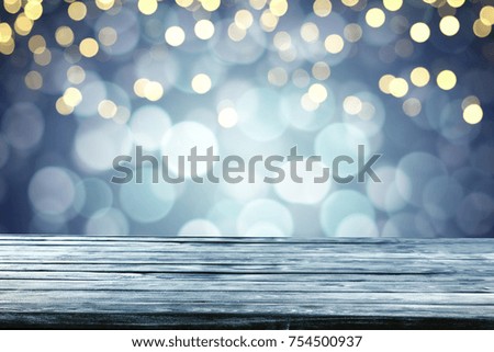 Desk with free space for your product. Blue Christmas background. Blurry Christmas lights in the background. Place for your advertising text.