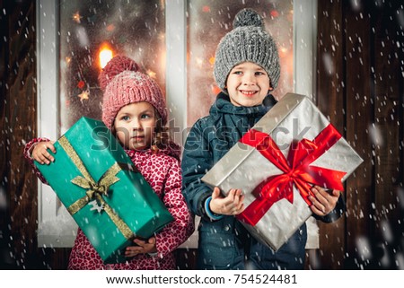 On Christmas night an adorable little boy  with his sister a girl with gifts in hand near the window the snow falls. They are waiting for Santa Claus.