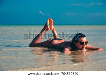 Young woman lying in water. Girl sunbathing in bikini and relax, enjoying life, lifestyle. Exotic tropical beach. Summer vacation resort and tourism, luxury travel concept. Paradise holiday island