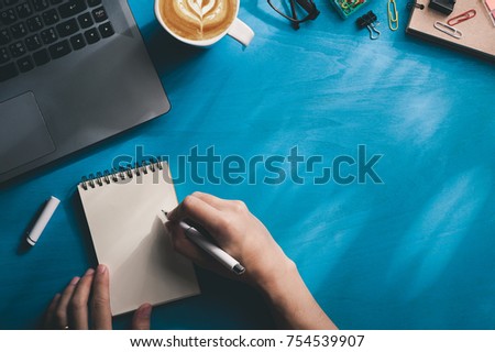 Young Asian male hand writing on small notebook on blue wood table in morning time with sunshine. Background with blank area for text or messages with photo filter effect