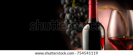 Red wine. Wine. Bottle and glass of Red wine with ripe grapes still life. Red wine Over black background. Wide angle Border art design with space for your text