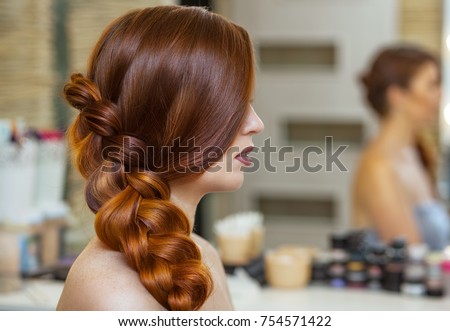Beautiful girl, with long, red-haired hairy. hairdresser weaves a French braid, close-up in a beauty salon. Professional hair care and creating hairstyles. Royalty-Free Stock Photo #754571422