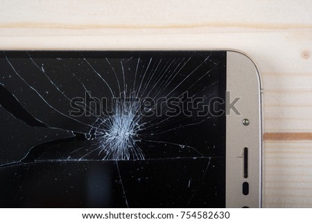 smartphone with broken pieces of the screen on a light wooden background