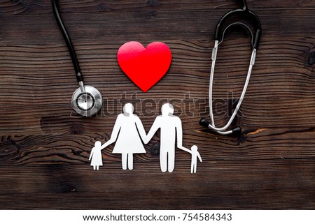 Choose family health insurance. Stethoscope, paper heart and silhouette of family on dark wooden background top view.