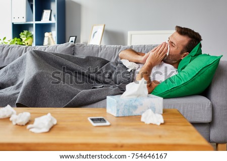 Sick man lying on sofa at home and blowing nose Royalty-Free Stock Photo #754646167