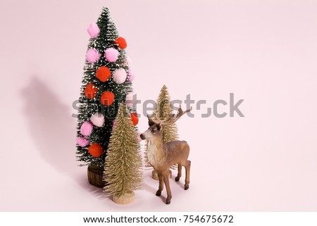 golden firs and decorated christmas tree with pompom with figurine reindeer next to it on a vibrant pink color background. Minimal still life photography