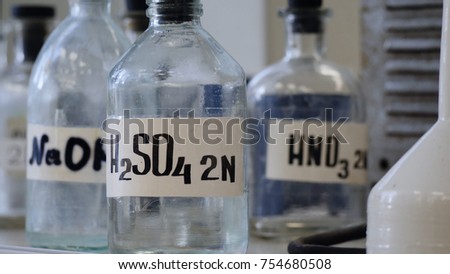 Bottles of solutions stored on shelf in laboratory. Bottles with chemical solutions of NaOH, H2so4 and HNO3. Sulfuric acid, sodium hydroxide, nitric acid Royalty-Free Stock Photo #754680508