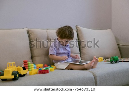 Toddler boy playing with digital tablet on couch at home