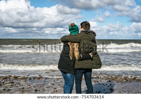 a young couple in love spending weekends on the coast of the cold Baltic sea, sandy beach, warm jackets, family weekend man and woman running on the beach.