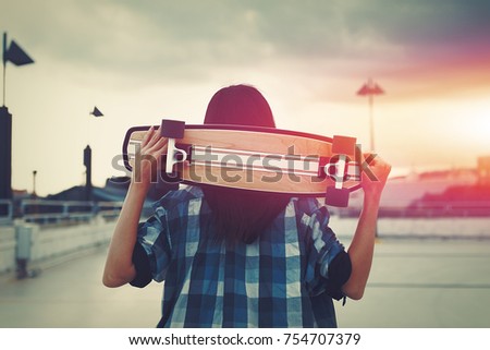 Young hipster woman holding skateboard behind head in sunset, outdoors, cinematic style, color graded