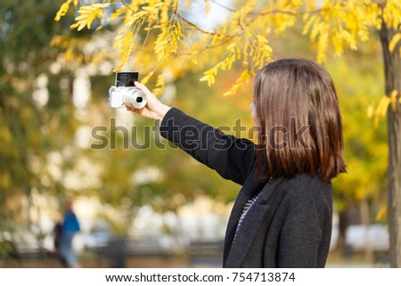 A girl in an autumn park makes selfie. View from the back.